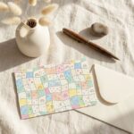Stationed postcard displaying a pastel patchwork pattern with hand-drawn rainbows, hearts, and flowers next to a blank address template.