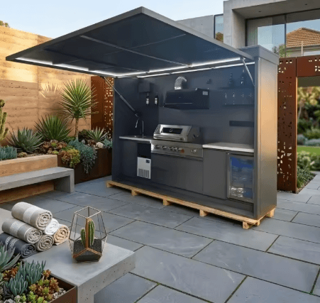 Modern American style outdoor kitchen pod with integrated gas grill, pizza oven, and fridge in a backyard patio.