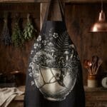 Black kitchen apron featuring vintage 19th-century botanical woodcut engraving of wild garden ferns, moss, and mushrooms in a gold kintsugi repaired bowl